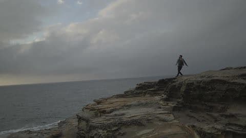 A Man Throwing Something from an Ocean Side Cliff on a Very Cloudy Day