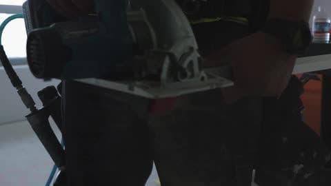 A Man Uses a Saw to Cut a Piece of Wood to Length