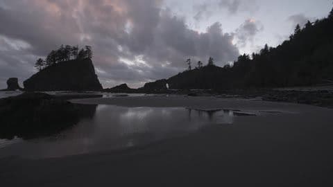 The Sandy Shore of a Body of Water Surrounded by Cliffs and Trees During a Very