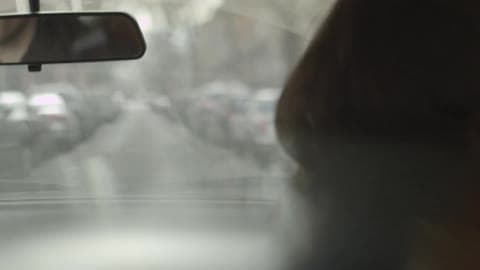 A Blonde Man Driving A Car Down A City Street