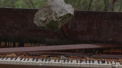 A Hand Throws A Large Rock Onto A Piano Outside In The Pouring Rain