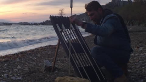 A Man Setting Up Fireworks On The Shoreline As Waves Crash To Shore On A Cloudy, Windy Evening
