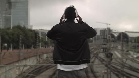A Man Stands High Above Train Tracks And Puts Head Phones Over His Ears