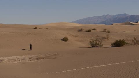 A Man Walking Through A Desert During The Day