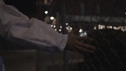 A Person Runs Hand Along A Chain Link Fence In The City At Night