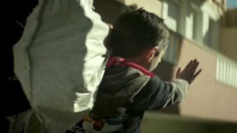 A Small Child Walking With An Adult Carries A Sack Over His Shoulder