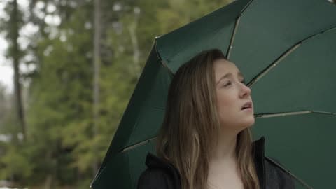 A Young Woman Holding An Umbrella And Walking Along A Tree Lined Path