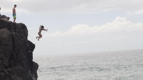 Girl Jumps Off A Rocky Cliff Into The Ocean Water
