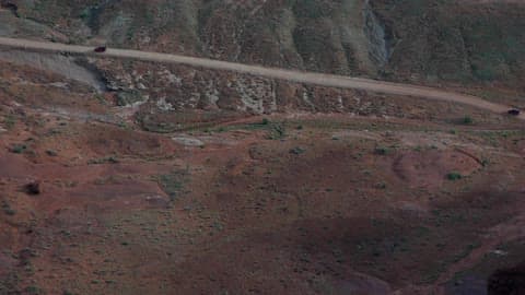 Two Jeeps Travel On A Sloped Dirt Road In A Desert Canyon