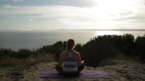 Woman Meditating On A Mat On The Beach