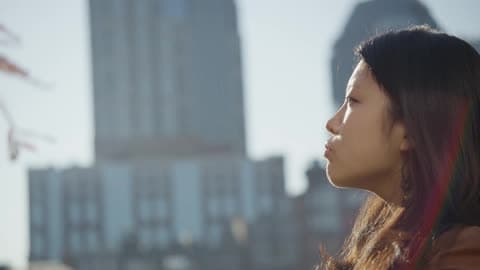 Woman Stares Into Distance With Buildings In The Background On A Cloudy Day